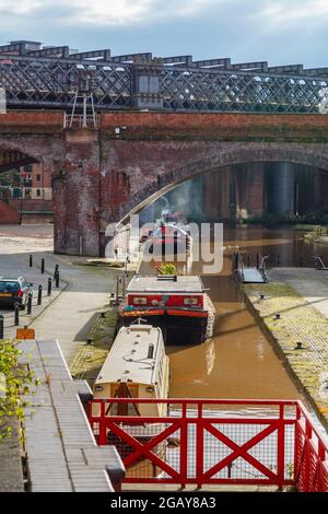 Narrowboote, die auf dem Bridgewater-Kanal durch einen Eisenbahnviadukt im Castlefield Urban Heritage Park, Manchester, Nordwestengland, Großbritannien, an der Schlepptau festgemacht werden Stockfoto