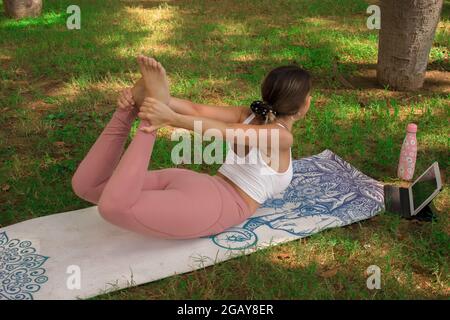 Vertikales Bild einer jungen Frau, die an einem sonnigen Sommertag im Stadtpark ein Video mit ihrem Tablet für soziale Medien macht. Pilates 2021 Stockfoto