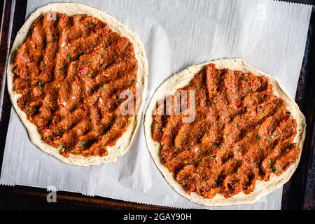 Zwei ungekochte türkische Lahmacun auf einer mit Pergamentpapier ausgekleideten Blechpfanne: Von oben aus Ansicht von rohen türkischen Fladenbroten mit gewürztem Hackfleisch Stockfoto