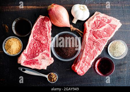 Gegrilltes NY Strip Steak mit Kaffeerub Zutaten: New York Strip Steaks, Rotwein, Kaffeesatz und Gewürze auf dunklem Holz Stockfoto