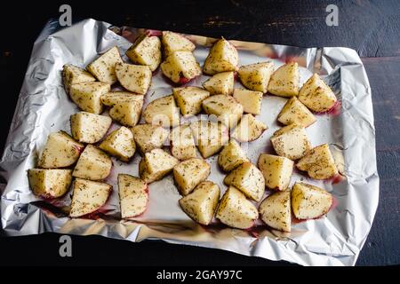 Rohe, gewürzte Kartoffeln auf einer mit Folie ausgekleideten Pfanne: Ungekochte rote Kartoffeln, die mit Olivenöl, Gewürzen und Knoblauch überzogen sind Stockfoto