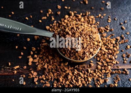 Instant Coffee in a Metal Measuring Löffel on a Dark Wood Background: Ein Messlöffel gefüllt mit Instant-Kaffee-Granulat, das auf verschüttet wird Stockfoto