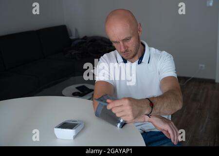 Mann fühlt sich schlecht. Er benutzte ein Blutdruckmessgerät zu Hause, um am Morgen seine Gesundheit zu überprüfen. Stockfoto