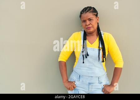 Seriöse afroamerikanische Frau, die sich an eine graue Wand lehnt Stockfoto