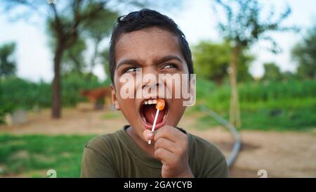 Frech indischen kleinen Jungen mit Süßigkeiten Bar. Süßer kleiner indischer/asiatischer Junge, der Eis/Mangobar oder Süßigkeiten isst. Isoliert über Naturhintergrund Stockfoto