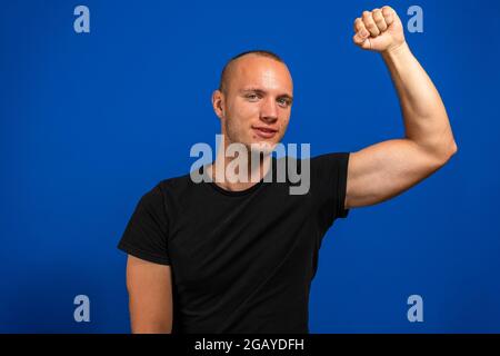 Foto von glücklichen siegreichen jungen Mann heben Hand feiern heben Faust isoliert auf blauem Hintergrund. Gewinner-Konzept. Stockfoto