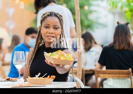 Nette Latina-Frau, die der Kamera Nachos und Guacamole anbietet Stockfoto