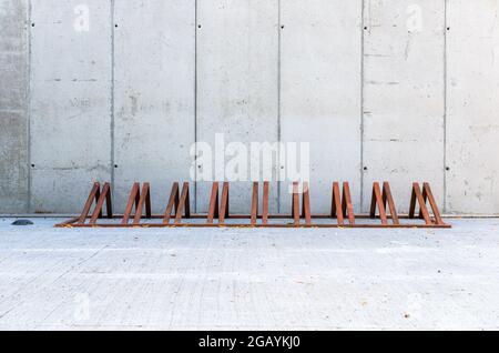 Row Moderne, leere Fahrradständer, aus rostfreiem Metall oder Cortenstahl. Betonwand im Hintergrund. Stockfoto