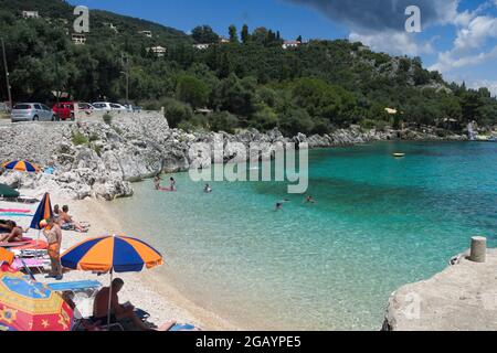 Nissaki, Korfu Griechenland Juli 10 2014 : farbenfroher Strand, in einer schönen kleinen Bucht mit Urlaubern, die sich in der Sommersonne entspannen. Nordostküste. Stockfoto