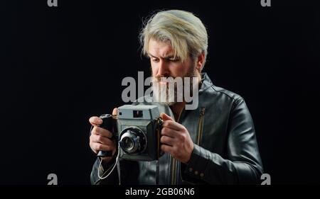 Bärtiger Mann mit Vintage-Fotokamera. Stilvoller Fotograf in Lederjacke mit Retro-Kamera. Stockfoto