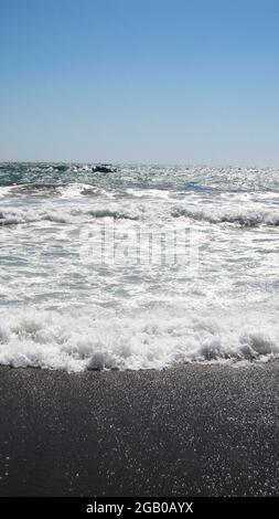 Wunderschöne blaue Meereswellen mit weißem Schaum aus nächster Nähe. Geschäftiges, heftiges Meer und Horizont im Hintergrund mit bewölktem, stürmischem Himmel. Minimalistisches Bild von Stockfoto