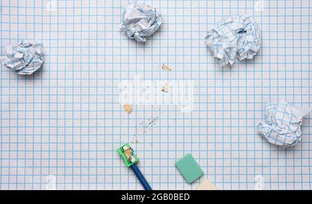 Zerknitterte Papierkugeln und ein geschärfter Holzstift mit Spalten auf einem karierten Papierblatt Stockfoto