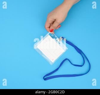 Weibliche Hand hält transparente Plastiktabzeichen auf einem blauen Lanyard auf blauem Hintergrund, Nahaufnahme Stockfoto