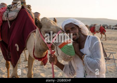 Al Wakrah, Katar - 13. Oktober 2019: Blick auf einen Einheimischen mit seinem Kamel im Kamelritt-Camp in Al W, einem Wahrzeichen für Wüstenaktivitäten Stockfoto