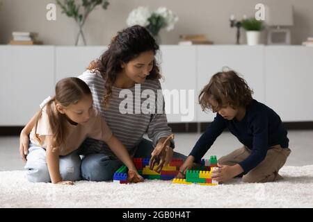 Junge Mutter und zwei Geschwister spielen zusammen auf dem Boden Stockfoto