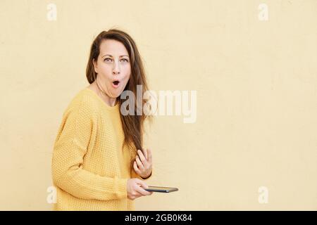 Frau chattet mit einem schockierten Gesichtsausdruck auf ihrem Smartphone, während sie in die Kamera schaut Stockfoto