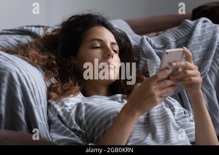 Faule gleichgültige Frau, die sich im Bett ausruht, mit dem Smartphone Stockfoto