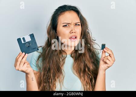 Junge hispanische Mädchen hält Diskette und sdxc-Karte ahnungslos und verwirrt Ausdruck. Zweifel Konzept. Stockfoto