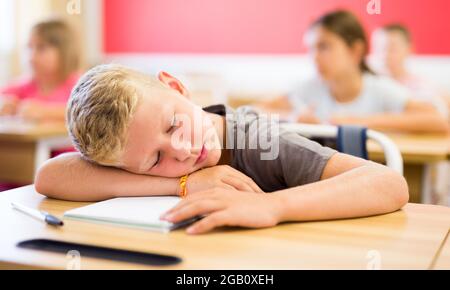 Müde präteen Schuljunge schlafen am Schreibtisch im Klassenzimmer Stockfoto