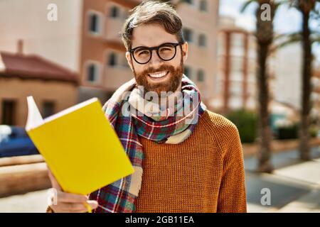 Junger Kaukasischer mit Bart und Brille beim Lesen eines Buches an einem sonnigen Tag Stockfoto