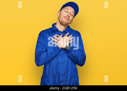 Glatze Mann mit Bart tragen Baumeister Jumpsuit Uniform lächeln mit Händen auf der Brust mit geschlossenen Augen und dankbare Geste auf dem Gesicht. Gesundheitskonzept. Stockfoto