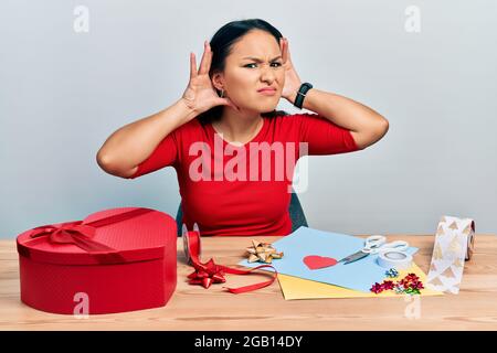 Schöne hispanische Frau mit Nasenpiercing tun Handwerk kreative Dekoration versuchen, beide Hände auf Ohr Geste hören, neugierig auf Klatsch. Hören Stockfoto