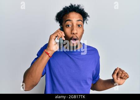 Junger afroamerikanischer Mann mit Bart, der auf dem Smartphone mit einem Gespräch sprach, erschreckt und erstaunt mit offenem Mund für ein überraschendes, ungläubisches Gesicht Stockfoto