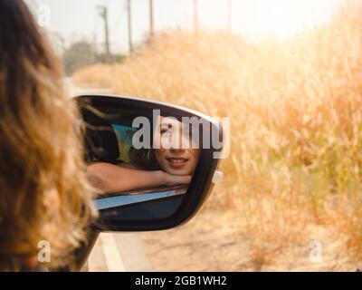 Glückliche asiatische Frau mit kurzen Haaren, die mit dem Auto unterwegs ist. Attraktive weibliche Reisende genießen und lächeln beim Blick auf die Aussicht draußen mit Sonnenschein, Sum Stockfoto