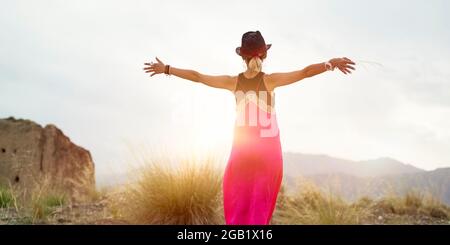 Rückansicht einer jungen asiatischen Frau in rotem Kleid, die das Morgenlicht in einem verlassenen Berggebiet umarmt Stockfoto