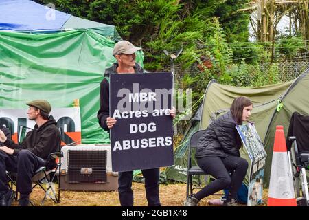 Huntingdon, Großbritannien. August 2021. Ein Demonstrator hält während des MBR-Acres-Protests in Huntingdon, Cambridgeshire, ein Anti-MBR-Acres-Plakat. Tierschutzaktivisten versammelten sich vor dem Beagle-Brutplatz von MBR Acres, um die Freilassung von 2000 Beagles zu fordern, von denen die Demonstranten behaupten, dass sie für grausame Experimente aufgezogen werden. Dutzende von Aktivisten haben auch außerhalb des Geländes ein langfristiges Camping eingerichtet, um das Unternehmen unter Druck zu setzen, die Hunde freizulassen und die Anlagen zu schließen. Kredit: SOPA Images Limited/Alamy Live Nachrichten Stockfoto