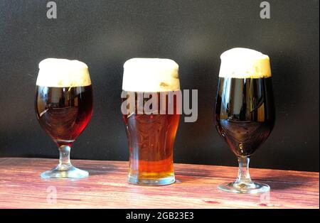 Auf einem Holztisch stehen drei Gläser mit verschiedenen dunklen Biersorten in einer Reihe. Nahaufnahme. Stockfoto