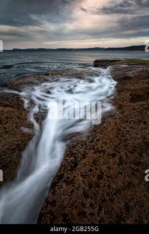 Wasser fließt von den Felsen in den Ozean entlang der Küste Stockfoto