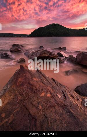 Atemberaubender, leuchtend rosafarbener Sonnenaufgang am Strand von den Felsen aus Stockfoto