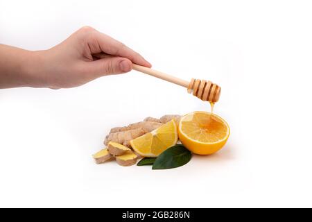 Die Hand einer Frau hält einen hölzernen Honiglöffel und gießt Honig über eine Zitrone. Isolierte Stücke von Ingwer und Zitrone mit Honig. Stockfoto