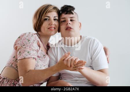 Mutter umarmt behinderten Jungen 17 Jahre alt im Rollstuhl mit zerebraler Lähmung auf weißem Hintergrund. Frau hilft Person mit besonderen Bedürfnissen. Emotional Stockfoto