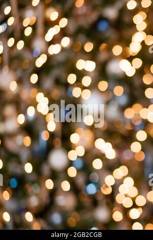 Goldenes Bokeh dekoratives Licht auf dem Weihnachtsbaum. Die Textur besteht aus einem kreisförmigen Bokeh, das aus verschwommenen orangefarbenen Glühbirnen im Holz entsteht. Stockfoto