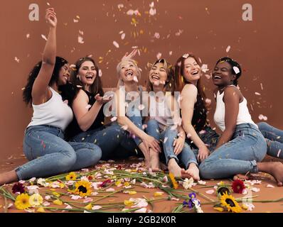 Eine multiethnische Gruppe glücklicher Frauen, die unter fallenden Blütenblättern sitzen Stockfoto