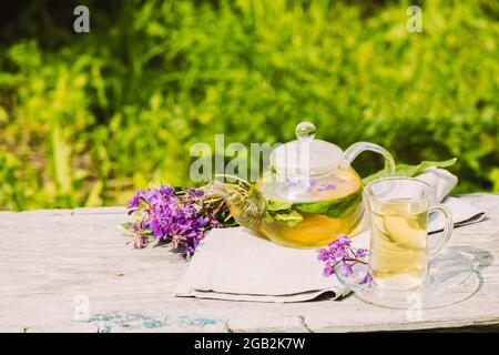 Tee mit frischen Zitronenmelisse Sommer Kräuter Kleeblätter in Glas Tasse und Teekannen auf Holz rustikalen Hintergrund Stockfoto