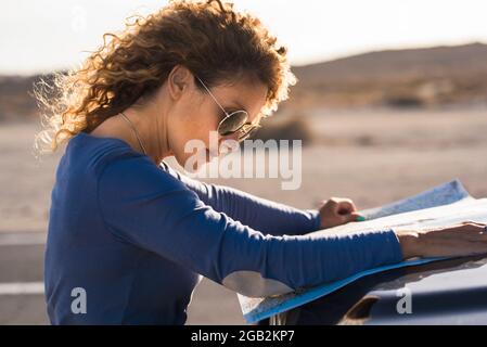 Erwachsene Frauen suchen Papier Reise Road Trip Karte auf dem Auto draußen mit Landschaft im Hintergrund - Konzept der weiblichen Menschen allein reisen mit Fahrzeug Stockfoto