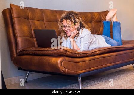 Erwachsene Frau legte sich auf das Sofa und benutzen Laptop-Computer lächelnd und Spaß allein zu Hause - Menschen weiblich und Internet Online-Surfen Aktivität Stockfoto