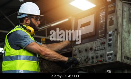 Maschinenbauingenieur, der in der Industrie und Fabrik mit reflektierender Schutzweste und weißem Helm arbeitet, Inspektor, der die industrielle Maschine im Stehen steuert und Stockfoto