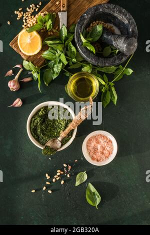 Pesto-Sauce in Schüssel mit Zutaten auf rustikalem grünen Tisch. Traditionelles italienisches Pesto-Rezept für Fettuccine, Pasta, Bruschetta. Stockfoto