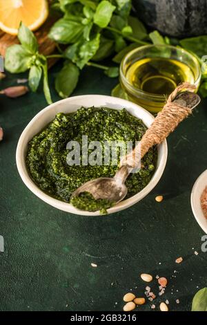 Pesto-Sauce in Schüssel mit Zutaten auf rustikalem grünen Tisch. Traditionelles italienisches Pesto-Rezept für Fettuccine, Pasta, Bruschetta. Stockfoto