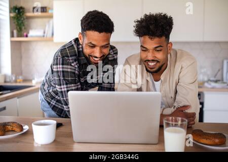 Junge Studentenbrüder, die zuhause in der Küche mit einem Laptop arbeiten. Stockfoto