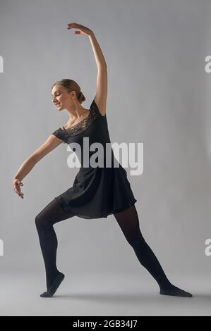 Die Tänzerin steht in einer Pose auf einem grauen Hintergrund Stockfoto