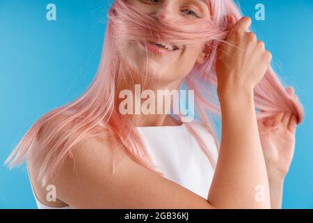 Portrait einer schönen weiblichen Model spielt mit rosa Haar, wickeln es um ihr Gesicht, während posiert isoliert über blauen Studio-Hintergrund Stockfoto