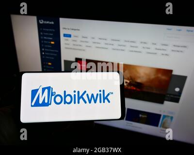 Person, die Mobiltelefon mit dem Logo des indischen Finanztechnologieunternehmens MobiKwik auf dem Bildschirm vor der Business-Webseite hält. Konzentrieren Sie sich auf die Telefonanzeige. Stockfoto