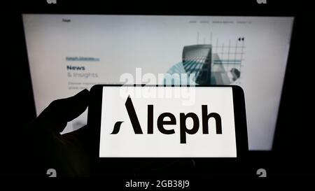 Person, die das Smartphone mit dem Logo des US-Digitalmedienunternehmens Aleph Holding vor der Website auf dem Bildschirm hält. Konzentrieren Sie sich auf die Telefonanzeige. Stockfoto