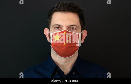 Mann trägt Chinise Flagge schützende medizinische Gesichtsmaske. Er sieht besorgt und besorgt aus. Coronavirus-Konzept in China mit schwarzem Hintergrund. Stockfoto