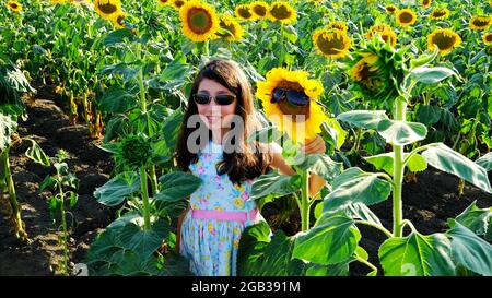 Ein schönes Mädchen grüßt die Sonnenblume und die Sonne. Stockfoto